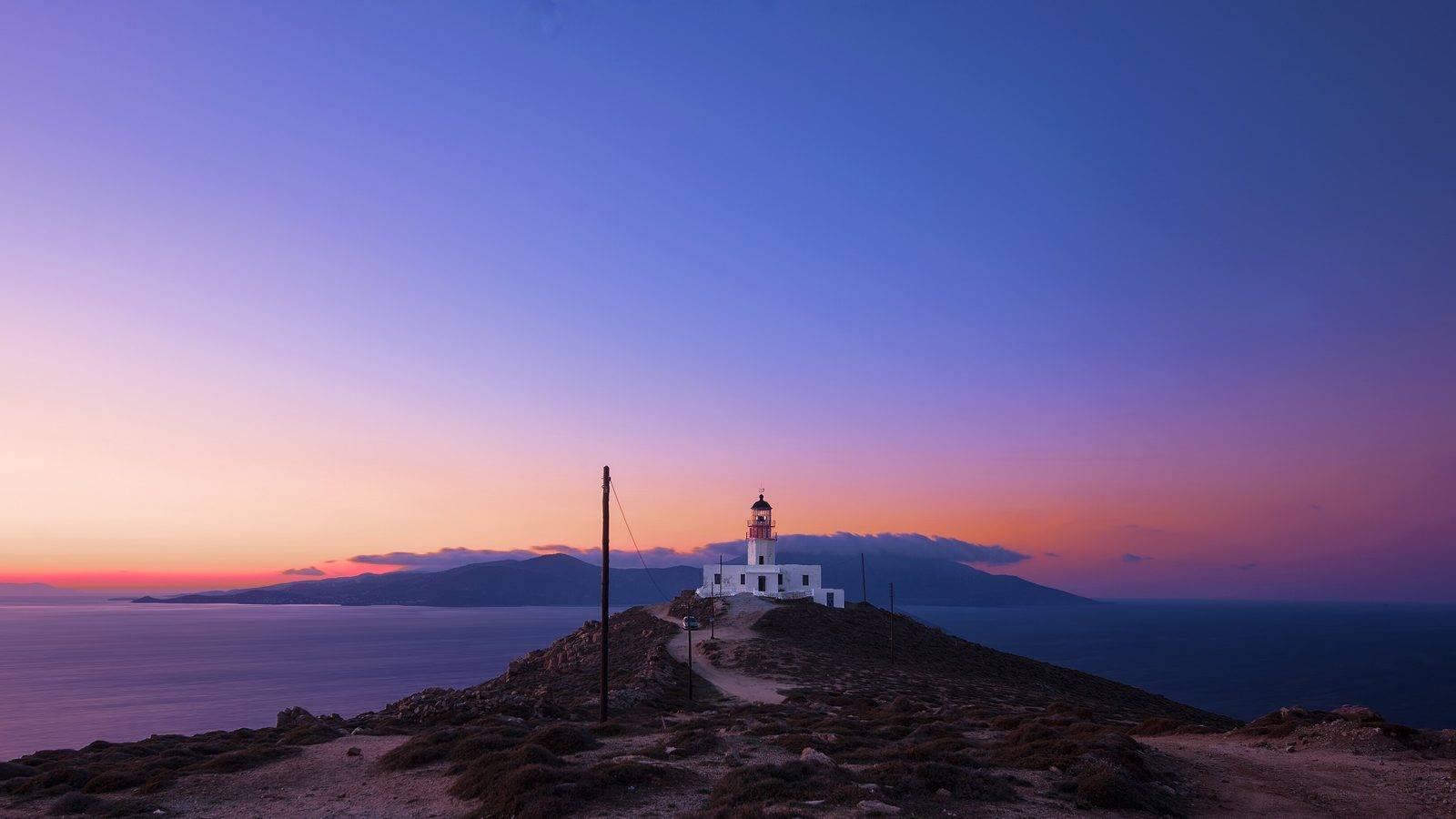 The Armenistis lighthouse in Mykonos at dusk, with the sky turning pink and violet over the Aegean